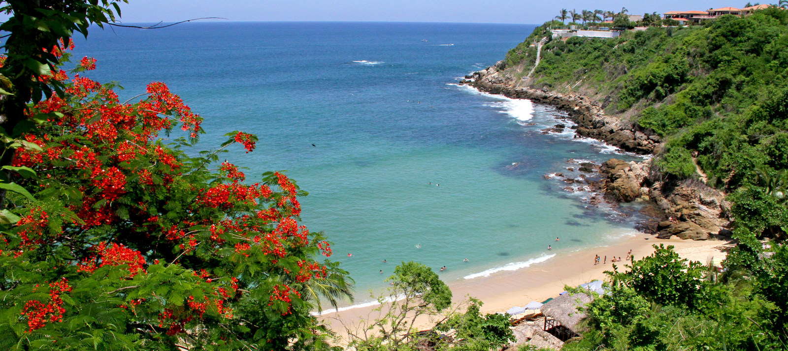 Scenic coastal view with a sandy cove beach, turquoise water, rocky cliffs, and lush green vegetation
