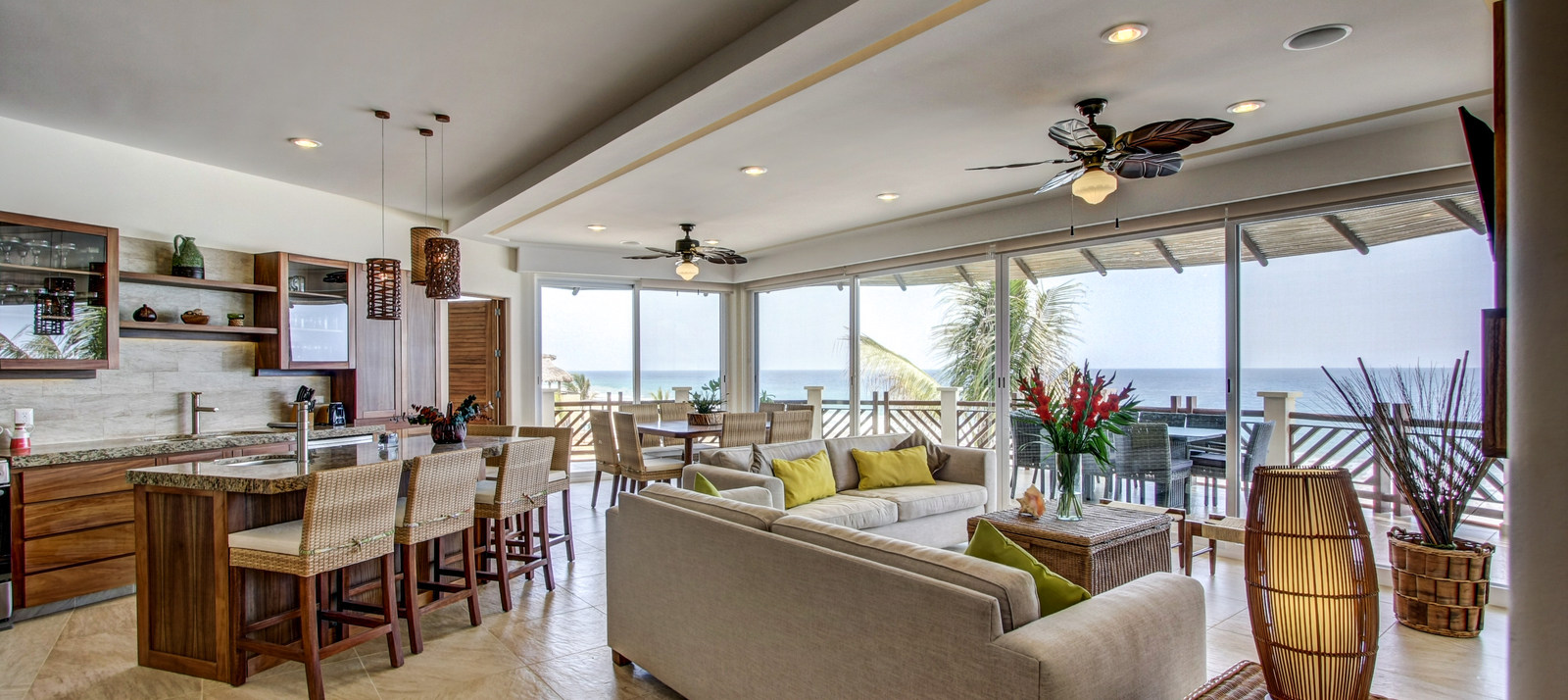 Bright open-concept living area with beige furniture, wooden accents, ceiling fans, and large glass doors opening to a patio